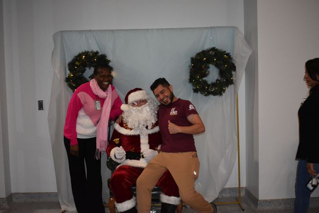 Santa seated between two people posing in front of a holiday backdrop with wreaths