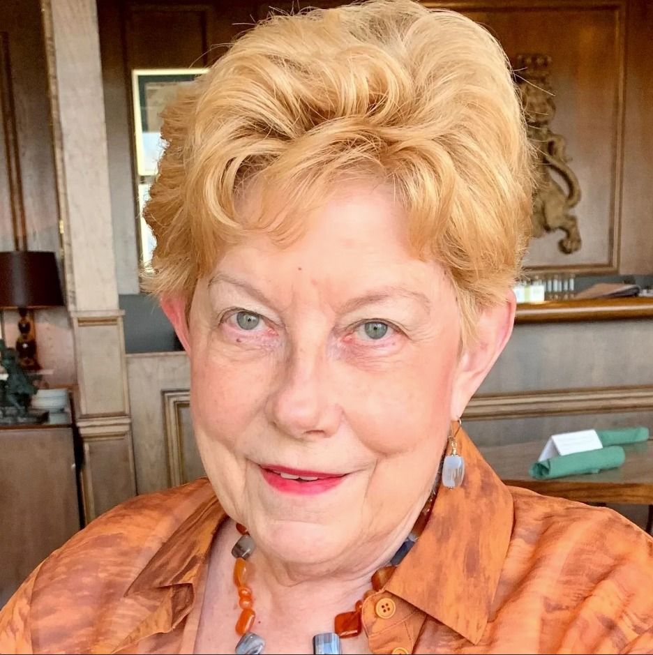 Woman with blonde hair and an orange shirt smiles. Indoors, warm lighting.