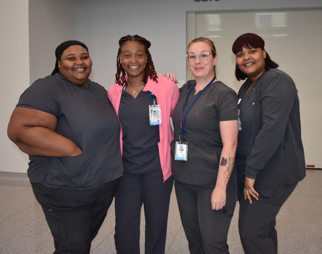 Four staff members in scrubs standing together indoors, smiling at the camera.