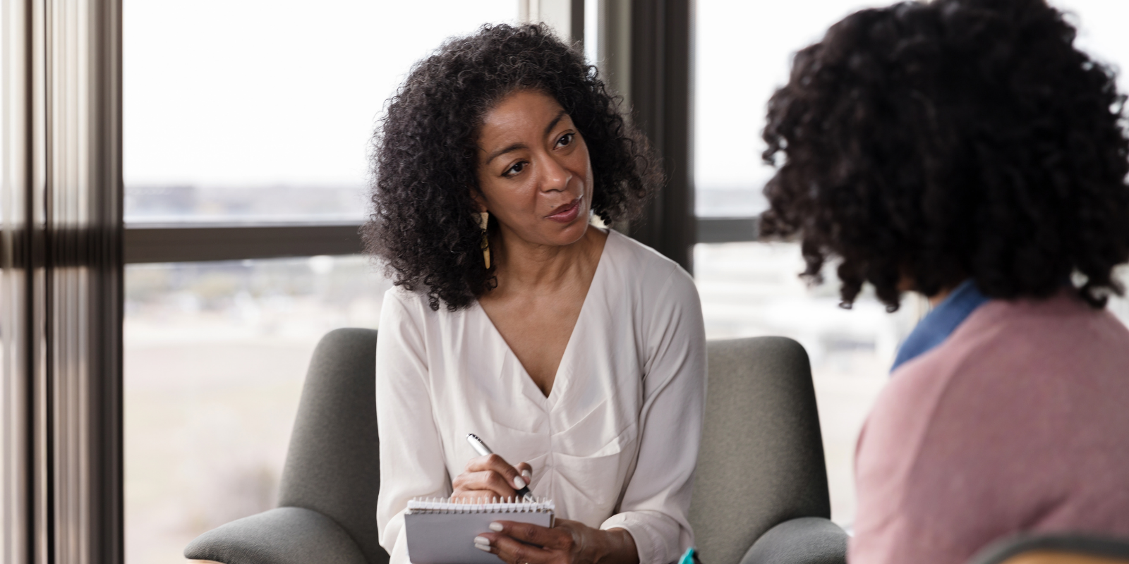 Two people talking in a bright office, one holding a tablet and listening attentively.