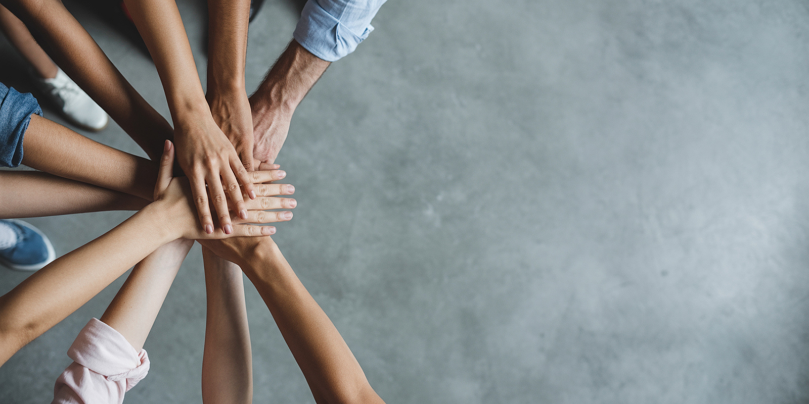 Hands stacked together in a team huddle on a gray background.