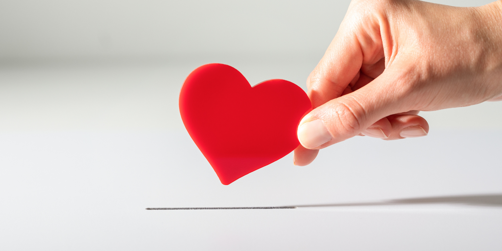 Hand holding a red heart above a thin line on a white background