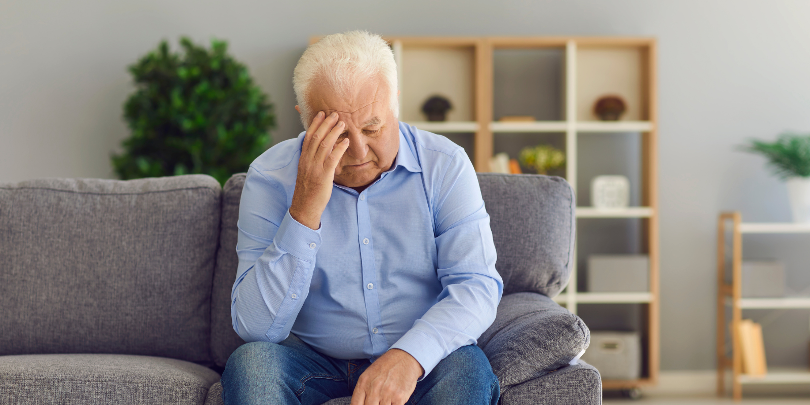 Person sitting on a couch, holding their head in a bright living room