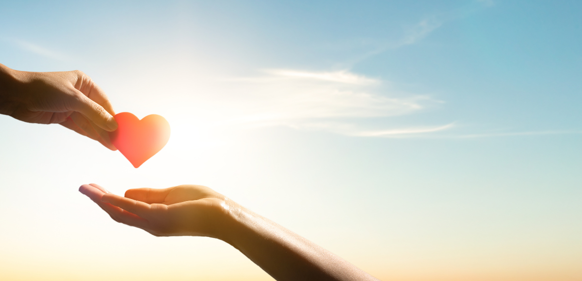 Two hands reaching toward a glowing heart at sunrise, symbolizing care and connection