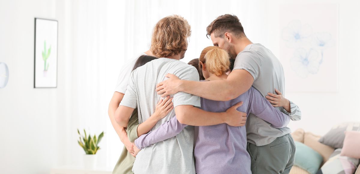 Four people hugging together in a bright living room