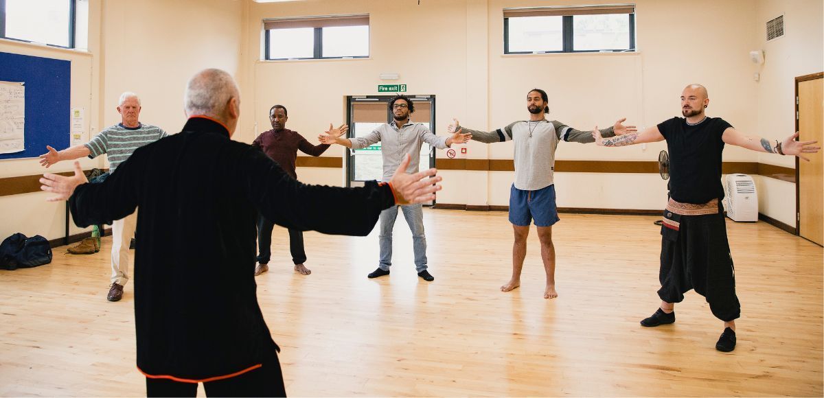 People exercising in a bright studio with arms extended during a group fitness class