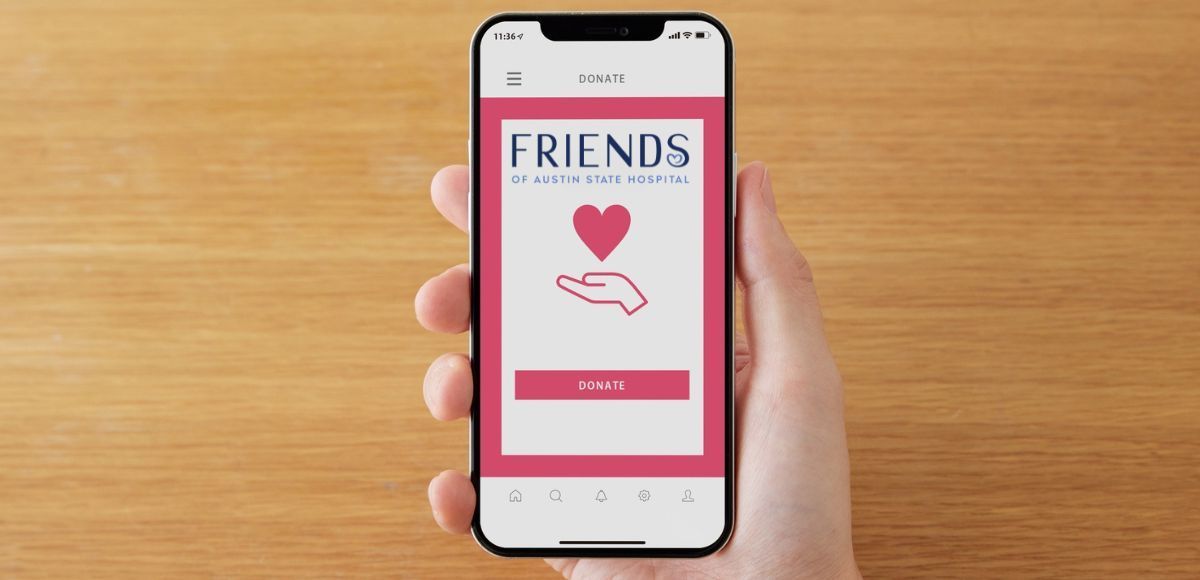 Hand holding smartphone showing a pink “FRIENDS” app screen with a heart icon and button