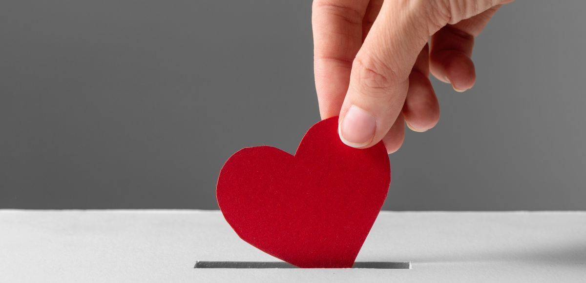Hand placing a red heart shape into a narrow slot on a white surface