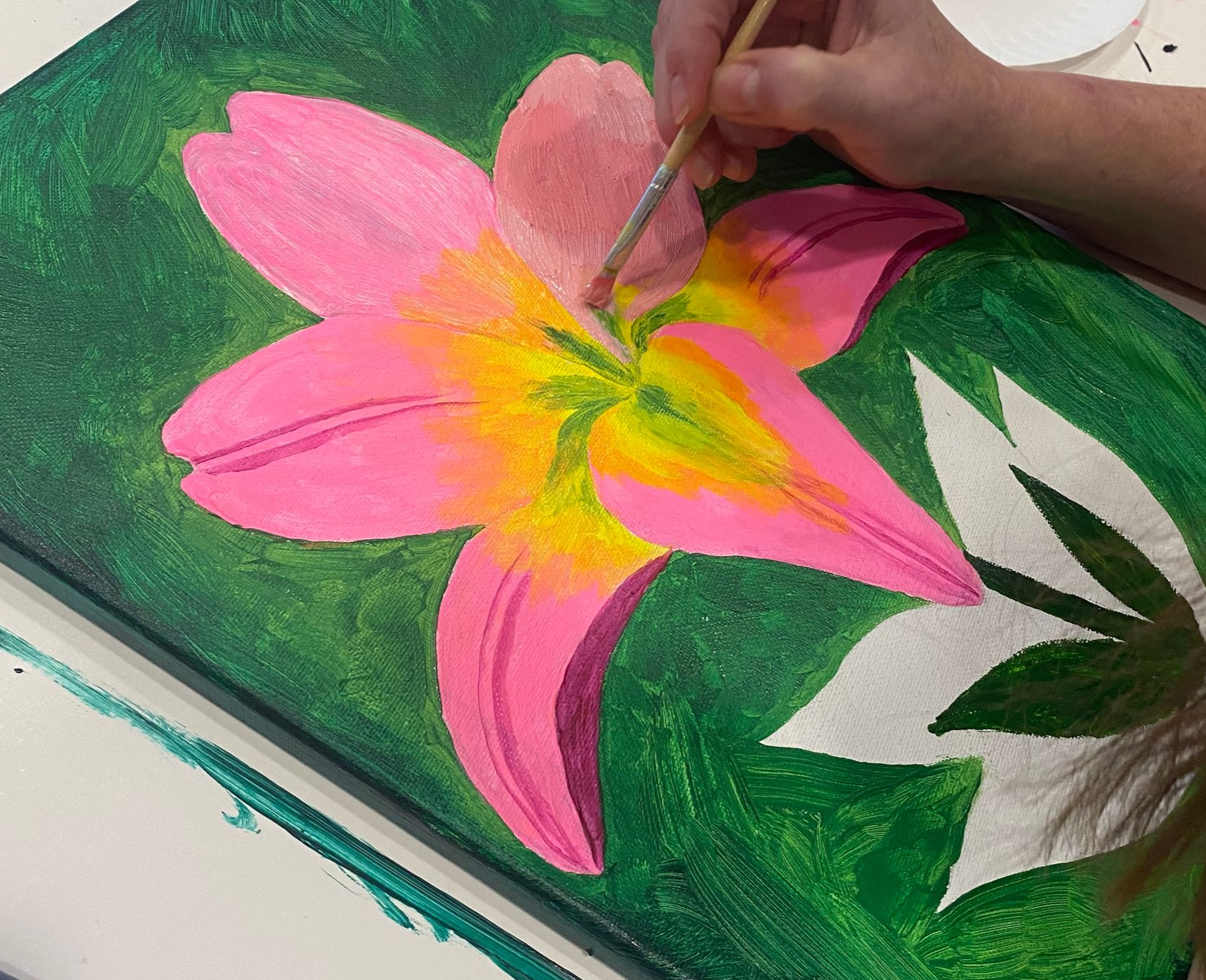 Hand painting a pink and yellow flower on green paper with a brush