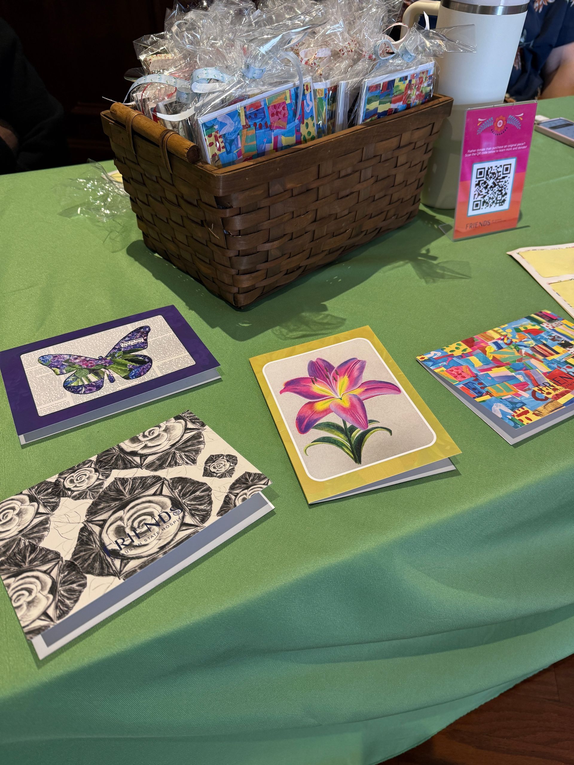 Handmade cards displayed on a green table beside a wicker gift basket filled with wrapped items.