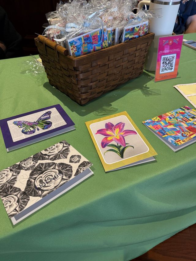 Handmade art cards displayed on a green tablecloth beside a basket of packaged items