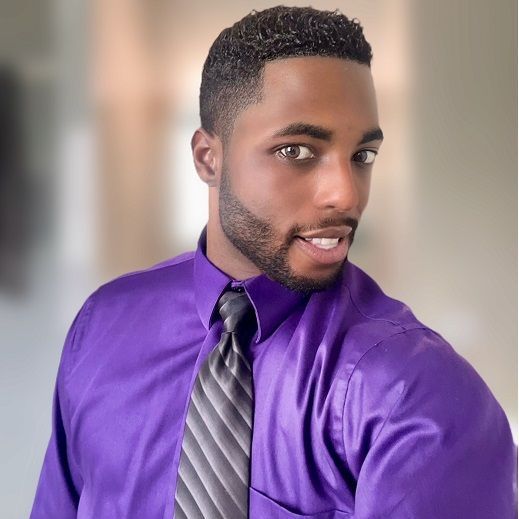 A man in a purple shirt and tie is smiling for the camera.