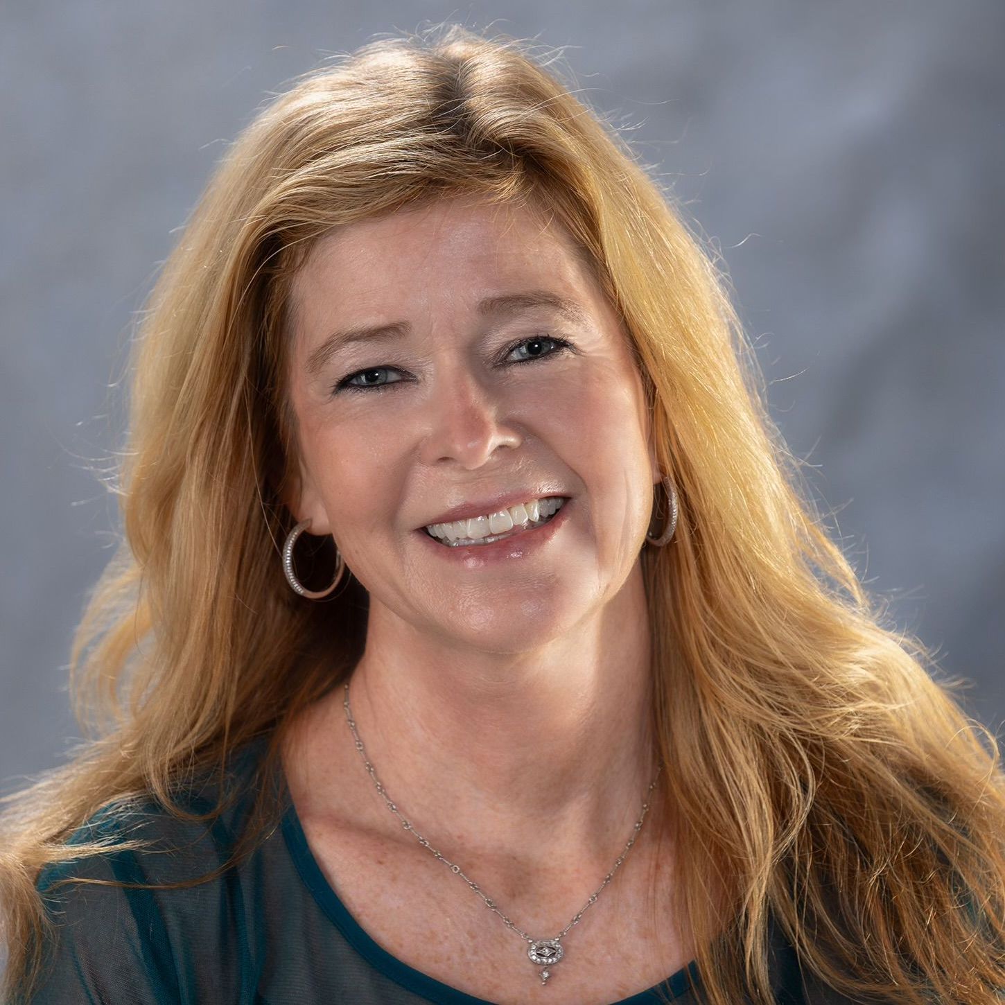 A woman wearing a necklace and earrings is smiling for the camera.