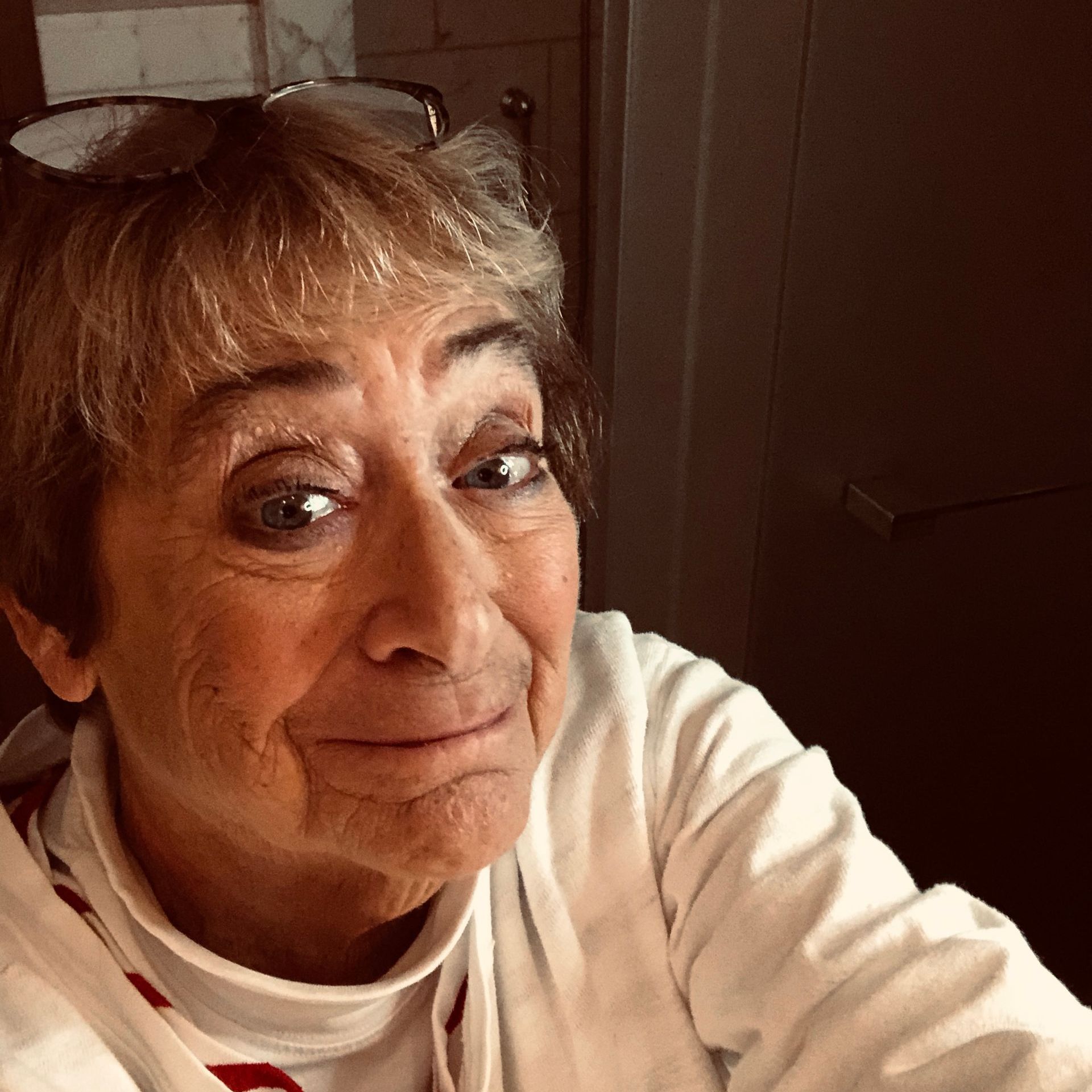 A woman wearing sunglasses and a white shirt is smiling