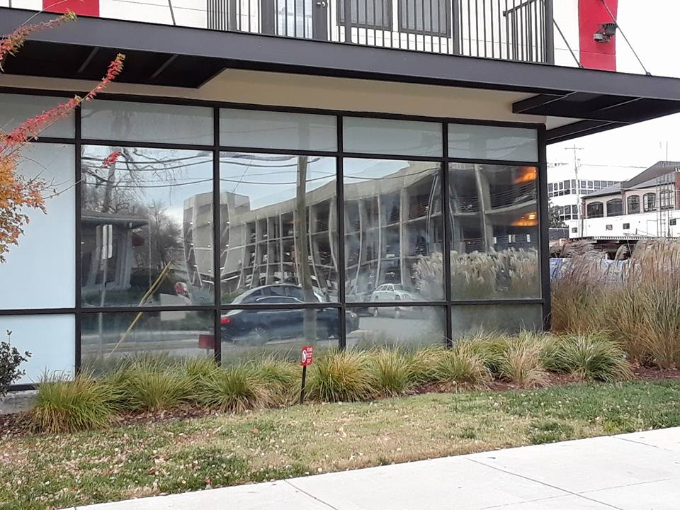 Modern building exterior with large glass windows, balcony, and landscaped shrubs in front