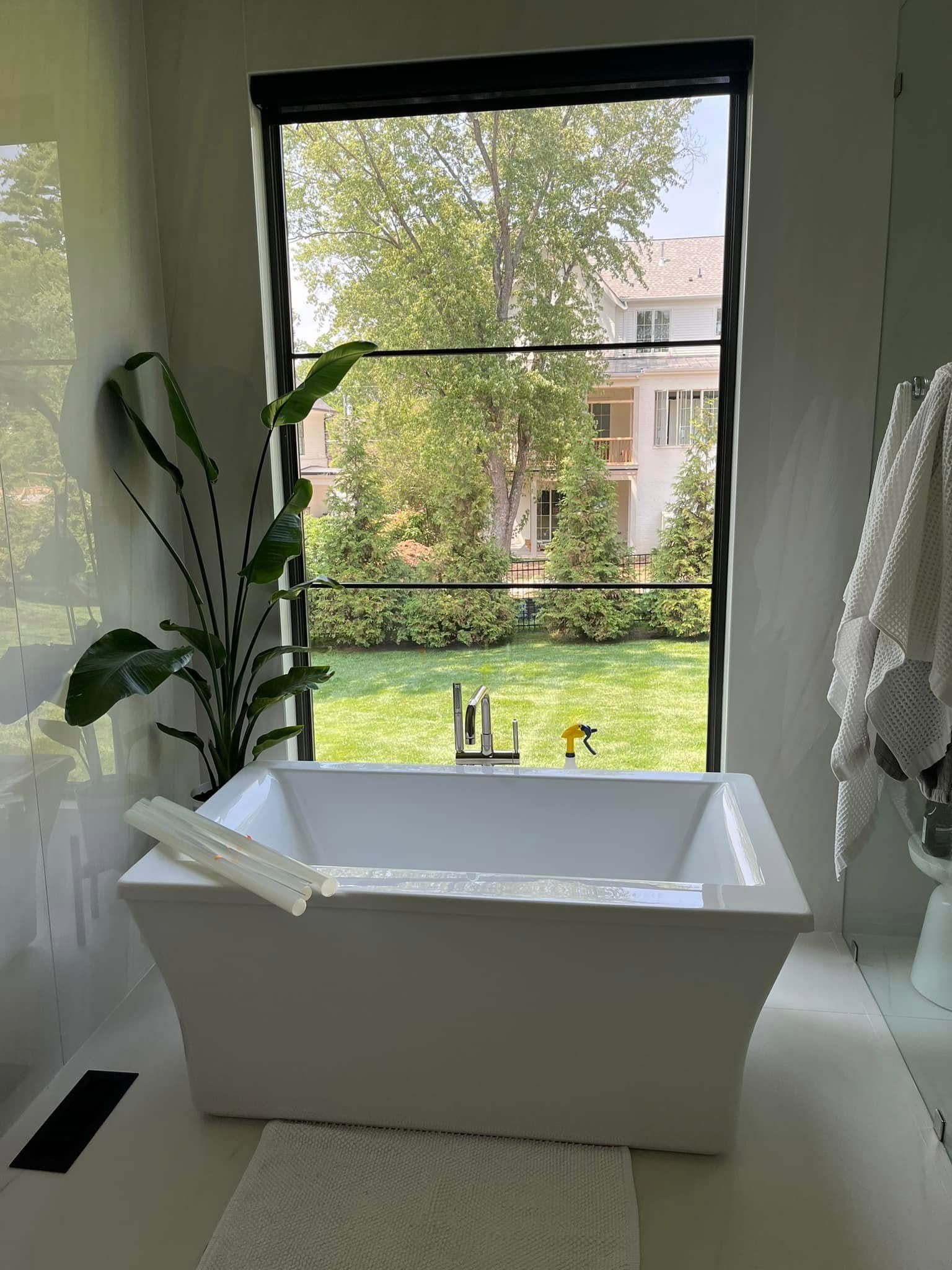 White bathtub by a large window with a garden view and potted plants nearby