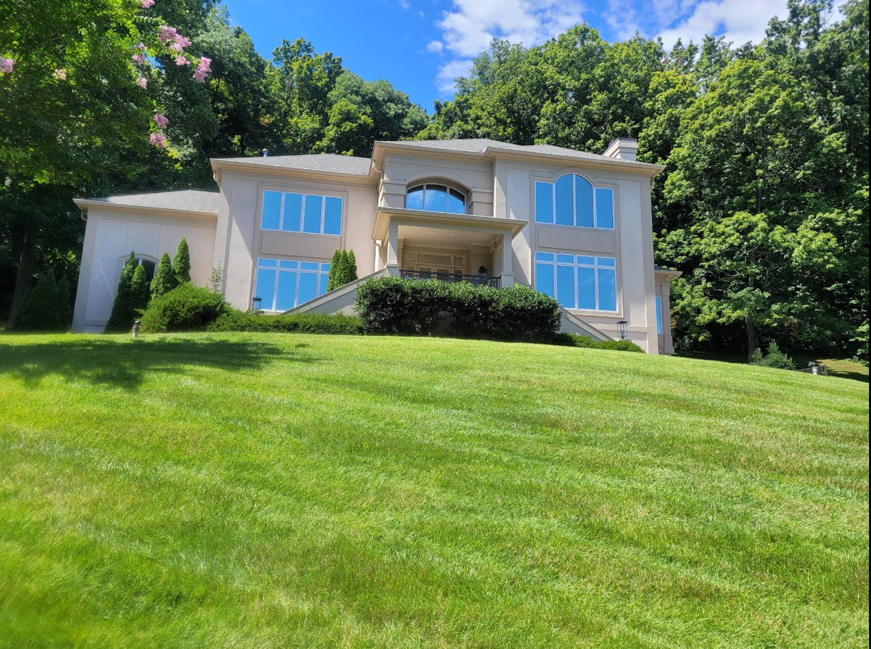 Large white house with blue windows on a grassy hillside under a bright blue sky