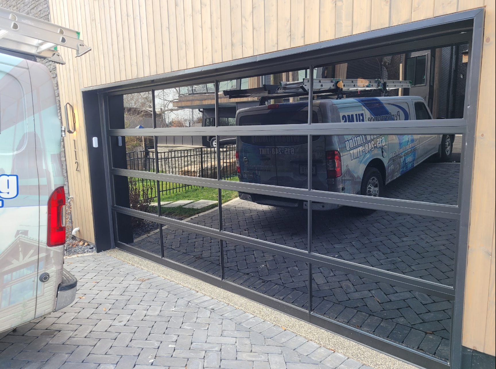 Black garage-style gate with reflective panels on a building wall, with a van visible inside.