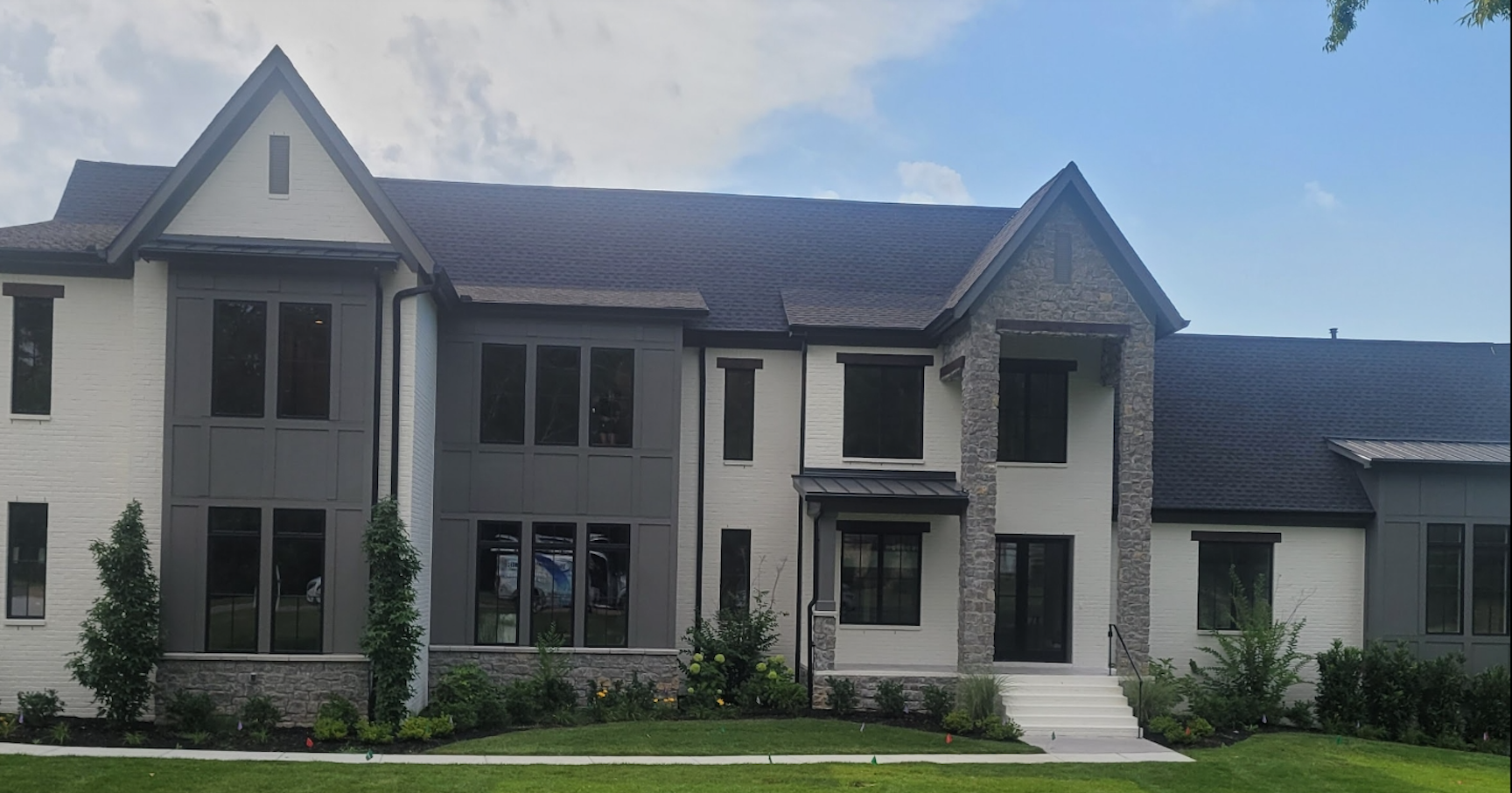 Large white two-story house with dark roof, tall windows, and a front lawn under a blue sky