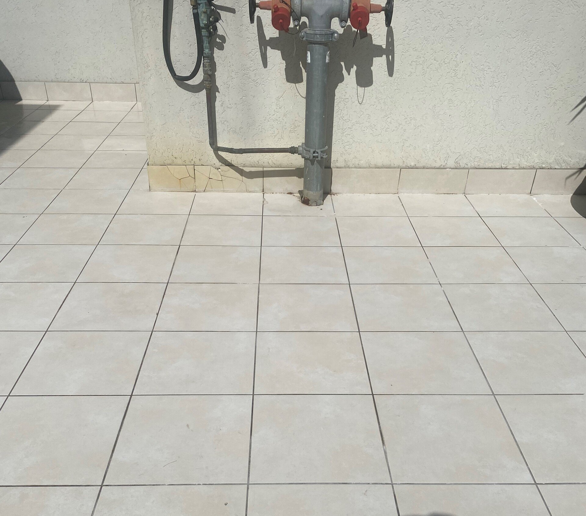 Beige tiled floor with fire hydrant against a beige wall.