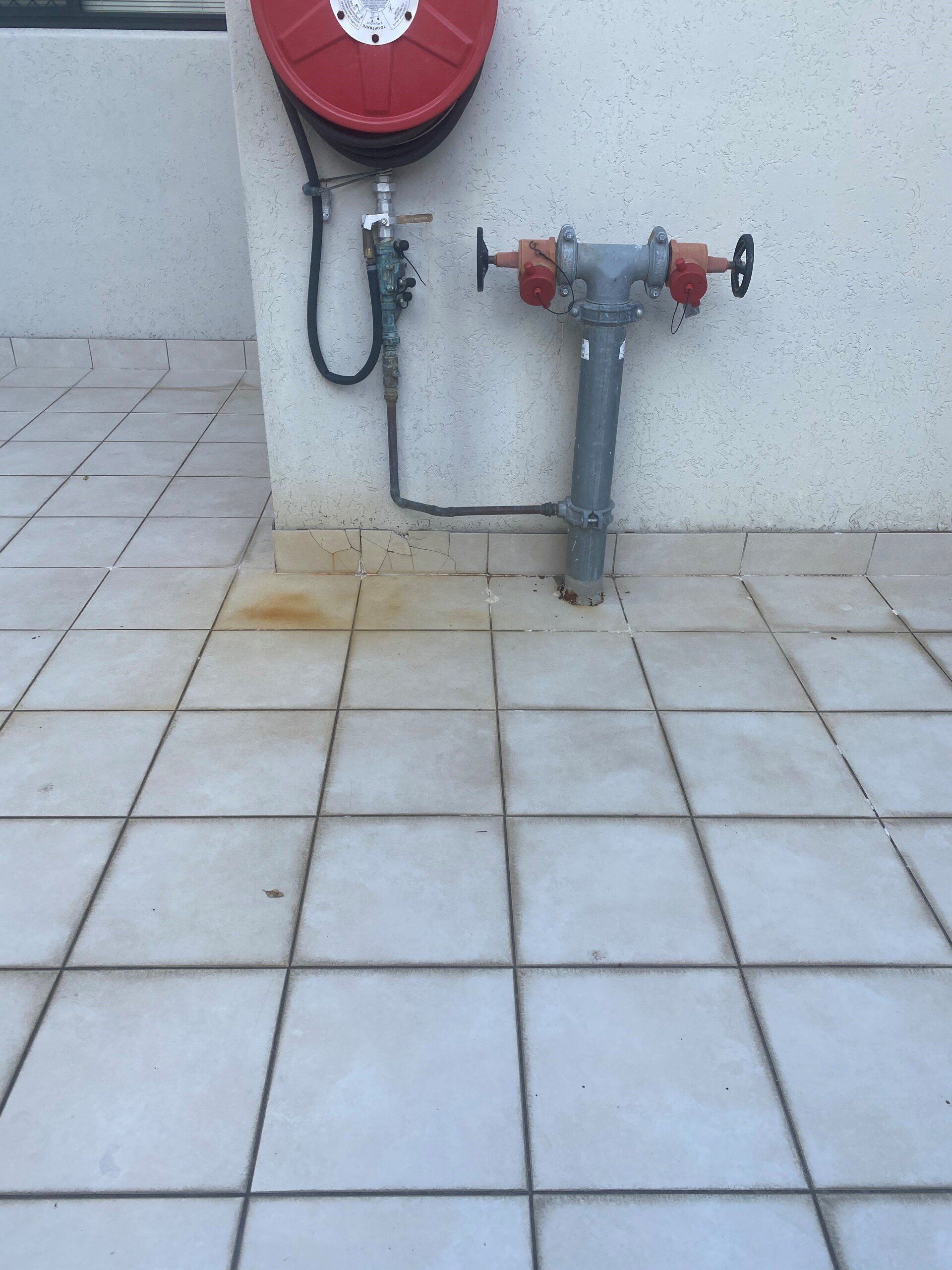 Fire hose reel and standpipe against a white tiled wall.