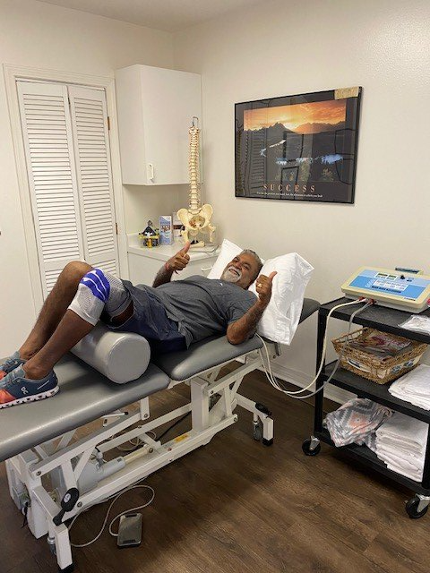 Patient lying on an exam table in a medical room, with a knee brace and ultrasound equipment nearby