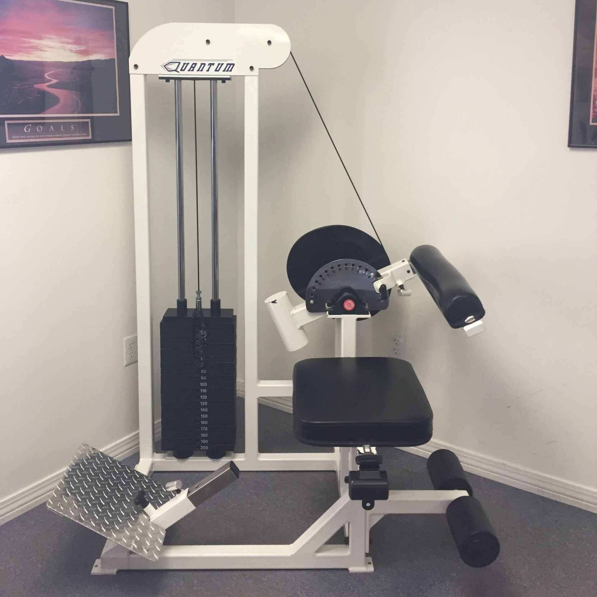 Leg extension exercise machine in a home gym room, with black padding and silver frame.