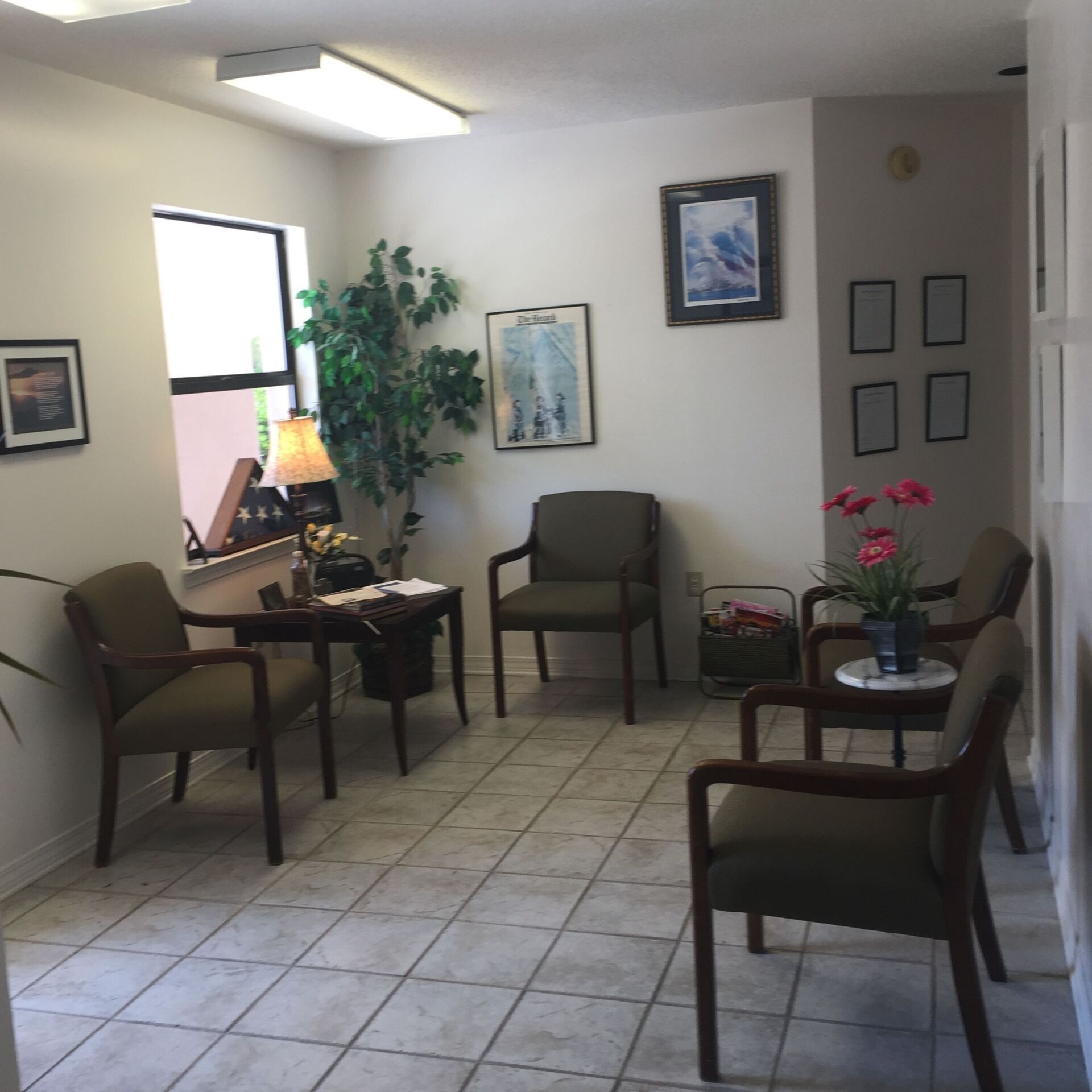Waiting room with chairs, tiled floor, lamps, and potted plants in a bright office corridor.