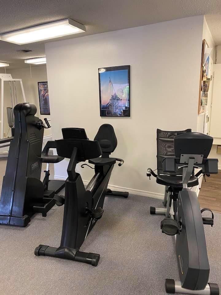 Gym room with three stationary bikes and a wall-mounted picture under bright ceiling lights