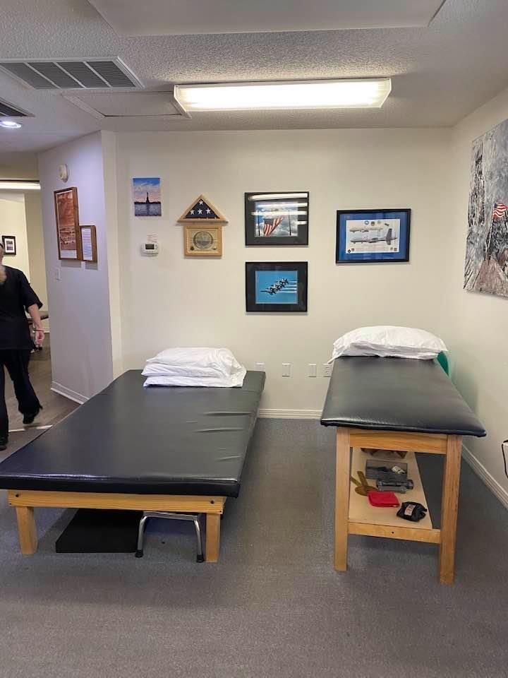 Treatment room with two black exam tables, framed wall art, and bright overhead lighting