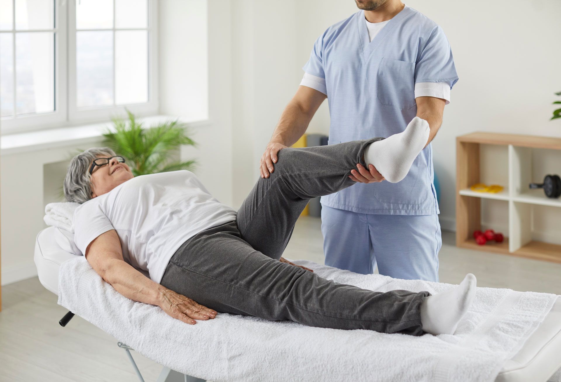 Caregiver stretching a patient’s leg on a treatment table in a bright therapy room