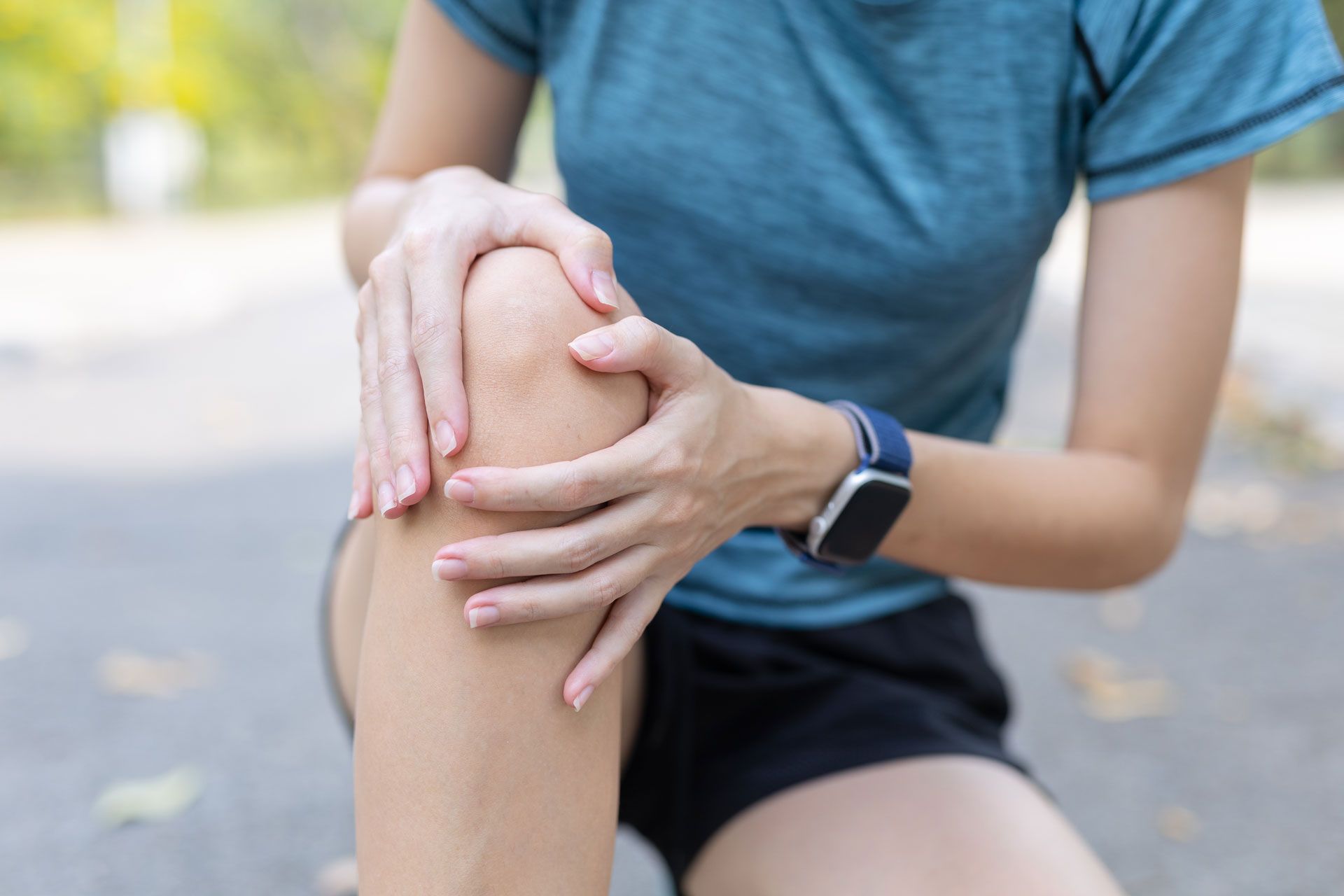 Person holding a knee with a fitness tracker, suggesting knee pain during outdoor exercise.