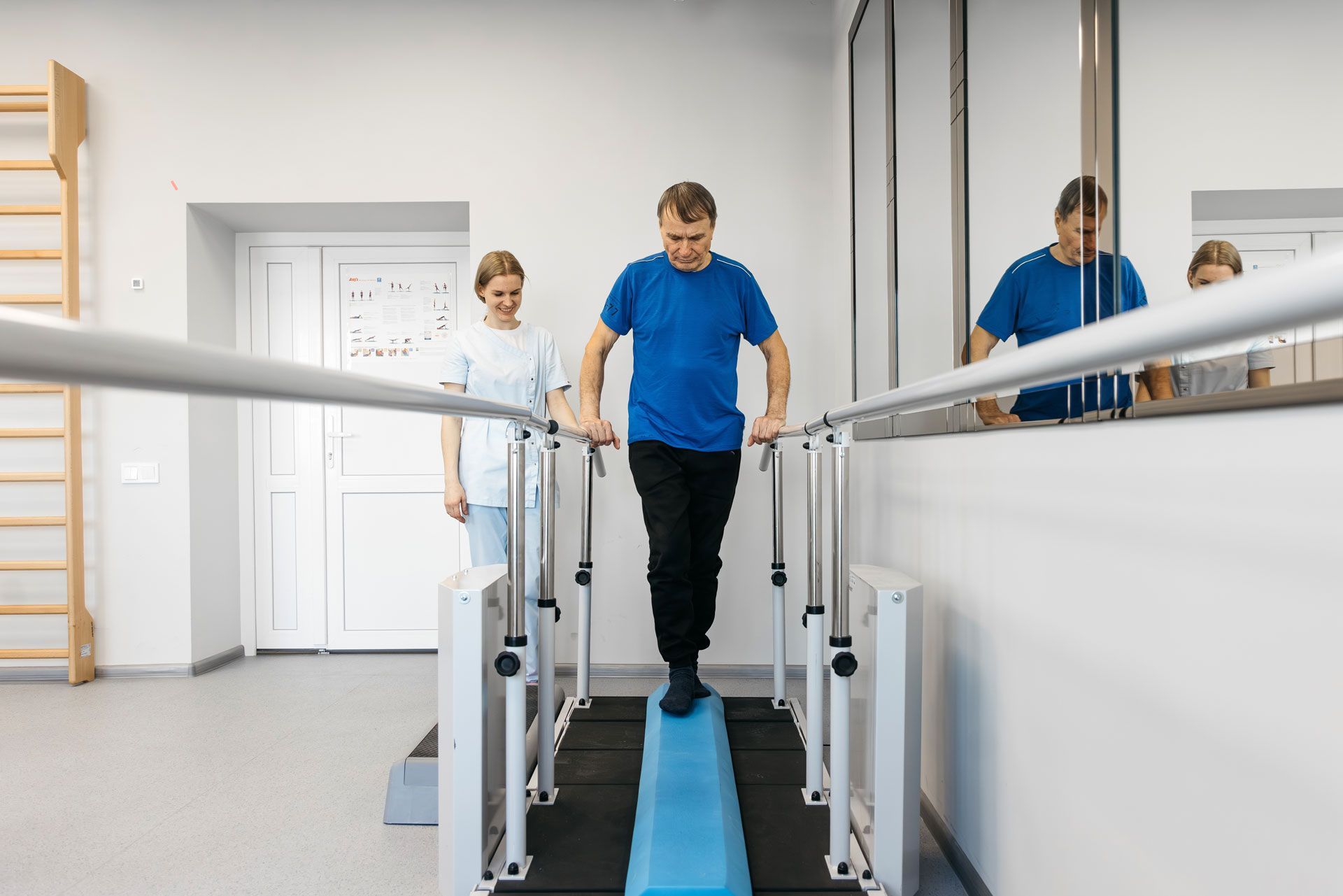 Person walking on a blue indoor therapy walkway with parallel handrails in a bright rehab room