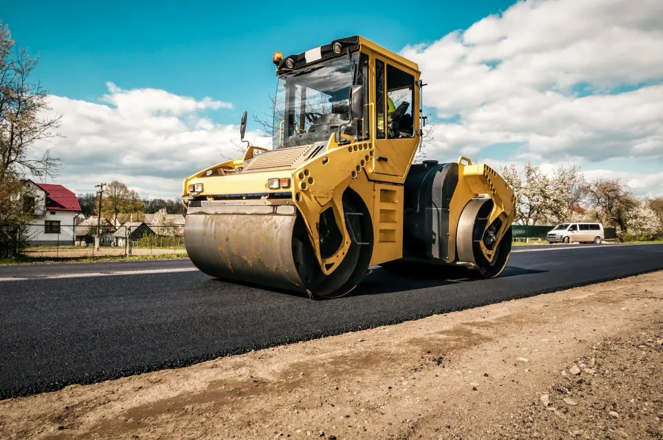A yellow road roller is driving down a road.