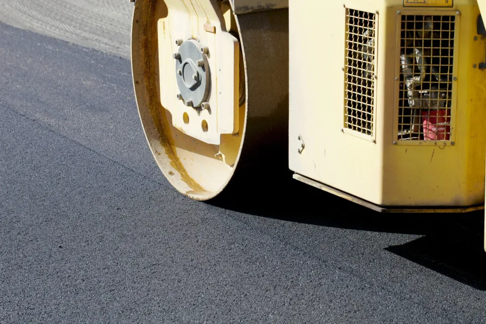 A yellow roller is rolling asphalt on a road.