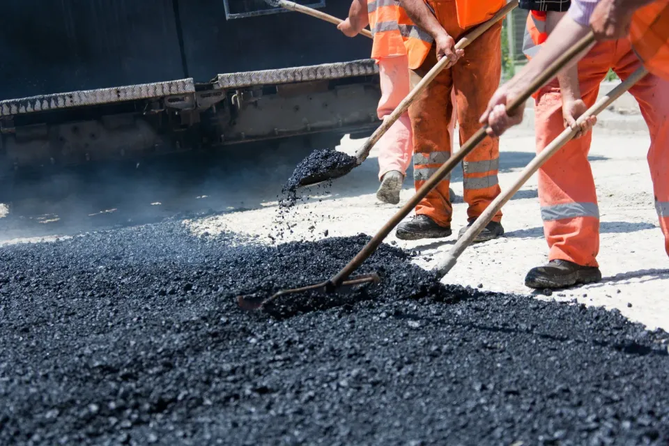 A group of construction workers are spreading asphalt on a road.