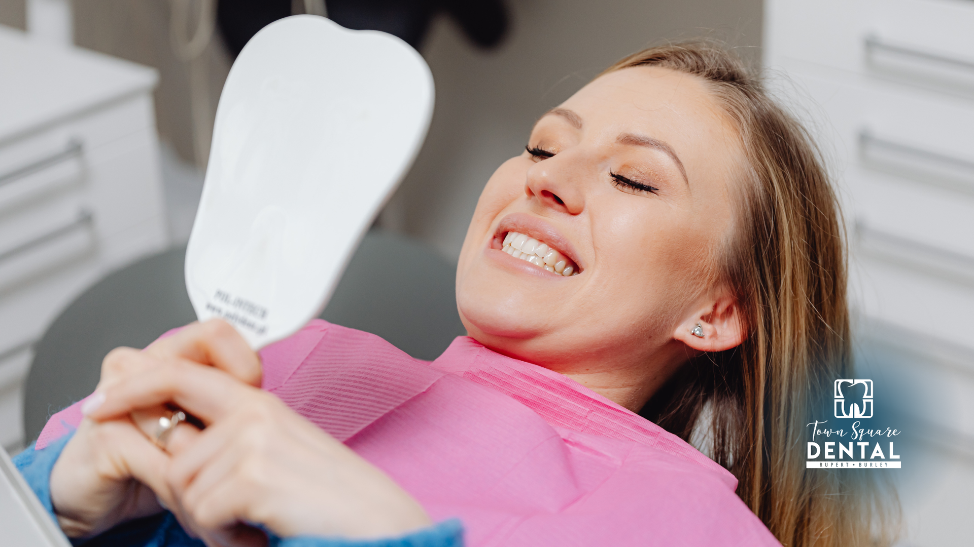 Smiling patient holding a dental mirror during a dental exam, with a dentist logo in the corner