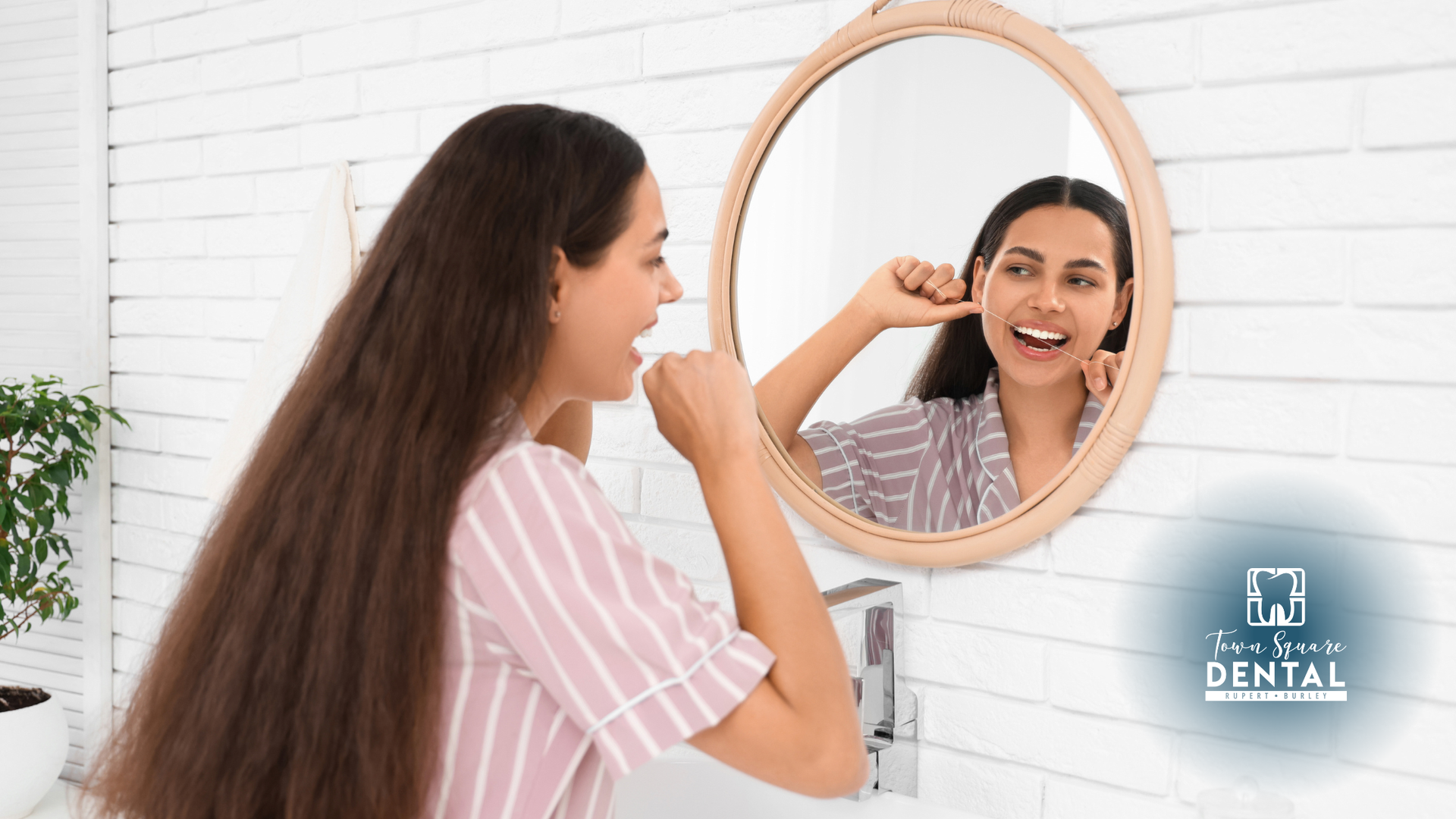Woman smiling in a mirror while flossing teeth in a bright bathroom