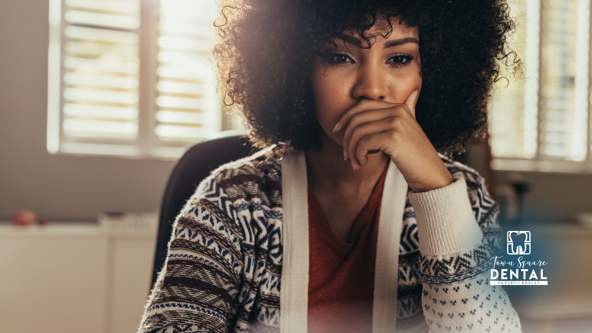 A woman is sitting at a desk with her hand on her chin.