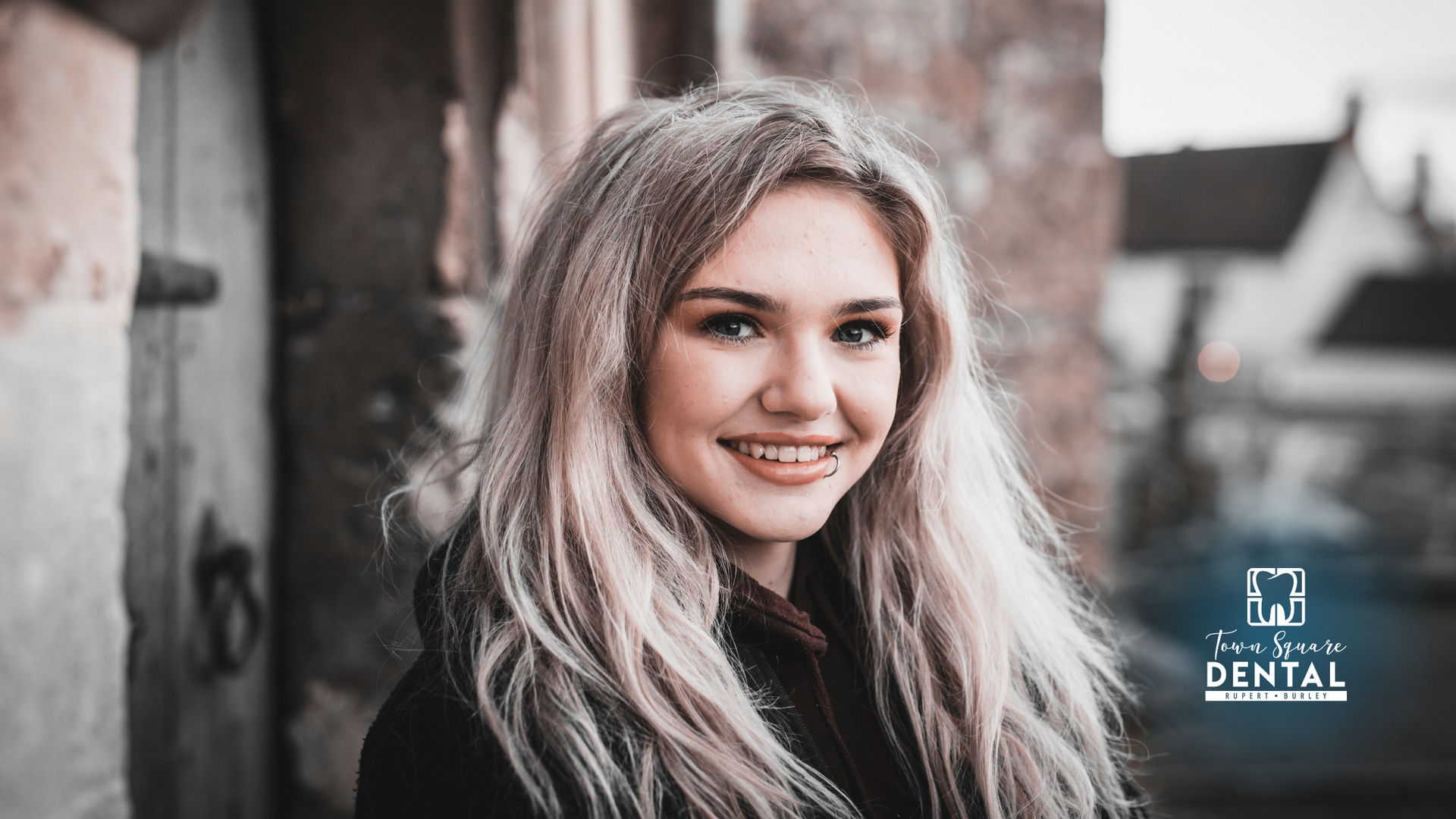 A woman with long blonde hair is smiling in front of a building.