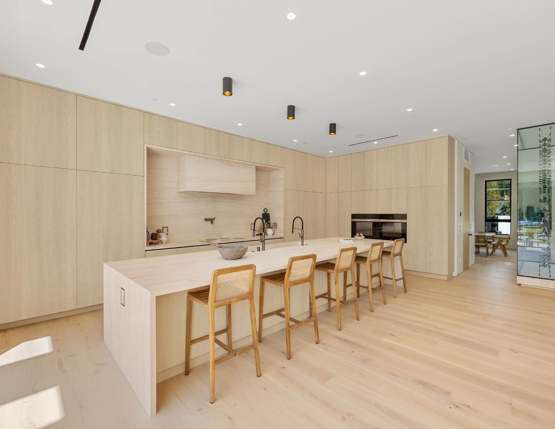 Modern kitchen with light wood cabinets, island with stools, and light wood flooring.