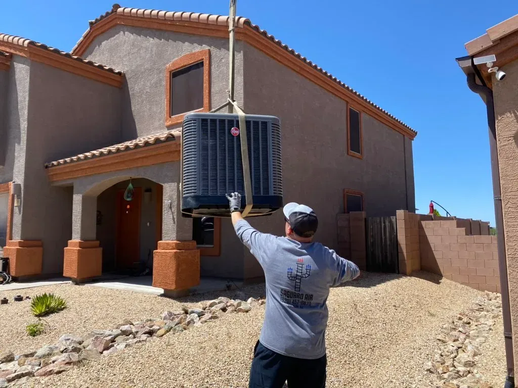 A man is lifting an air conditioner in front of a house.