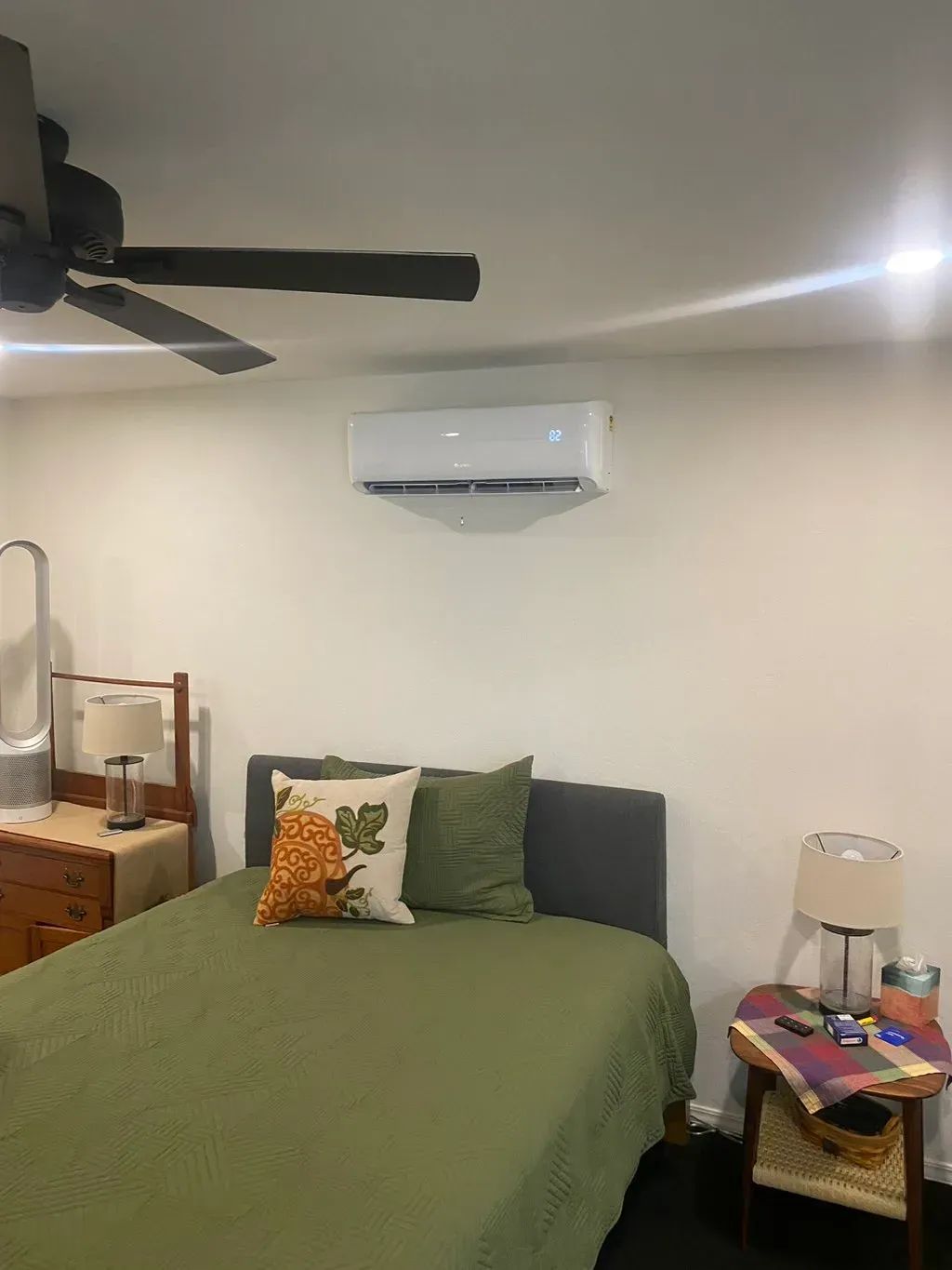 Bedroom with bed, air conditioner, and ceiling fan. Green bedding, white walls, and warm lighting.