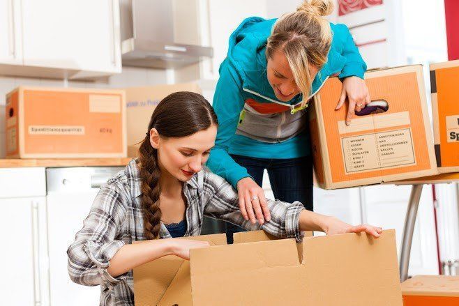 Two women are packing boxes together in a kitchen.