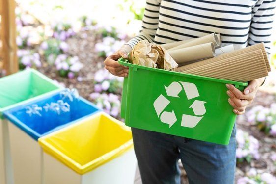 A woman is holding a green recycling bin full of recyclables.