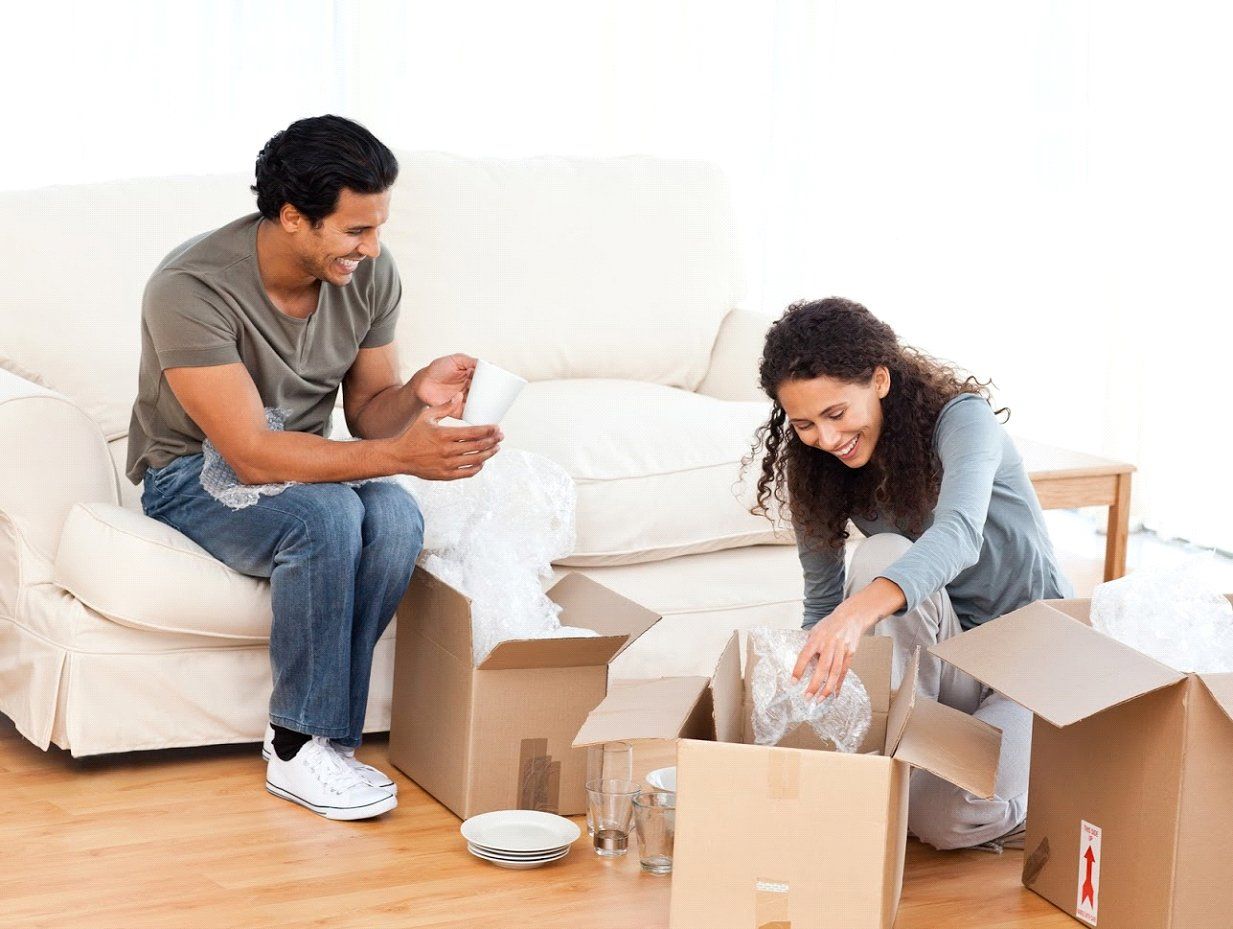 A man and a woman are sitting on a couch packing boxes.