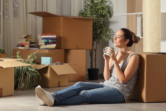 A woman is sitting on the floor drinking a cup of coffee.