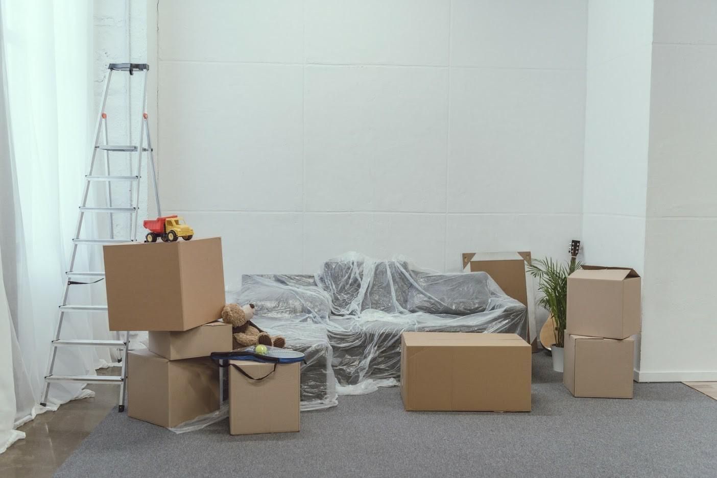 A living room filled with cardboard boxes and a couch covered in plastic wrap.