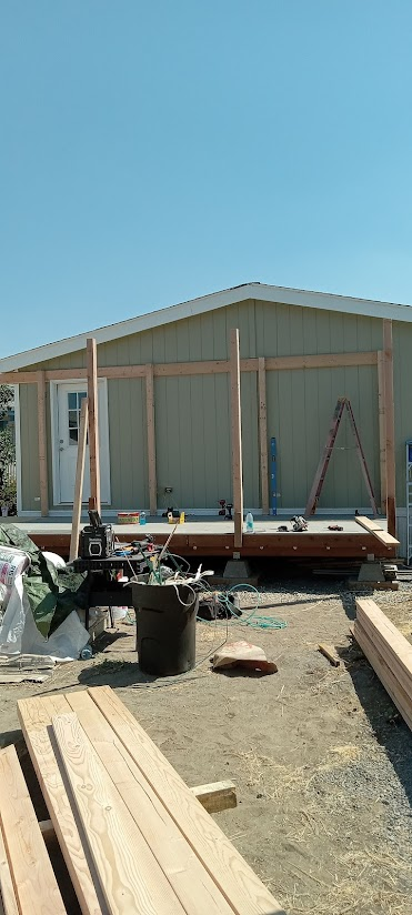 Construction of an outdoor porch on a light green building. Wooden beams and tools are visible.