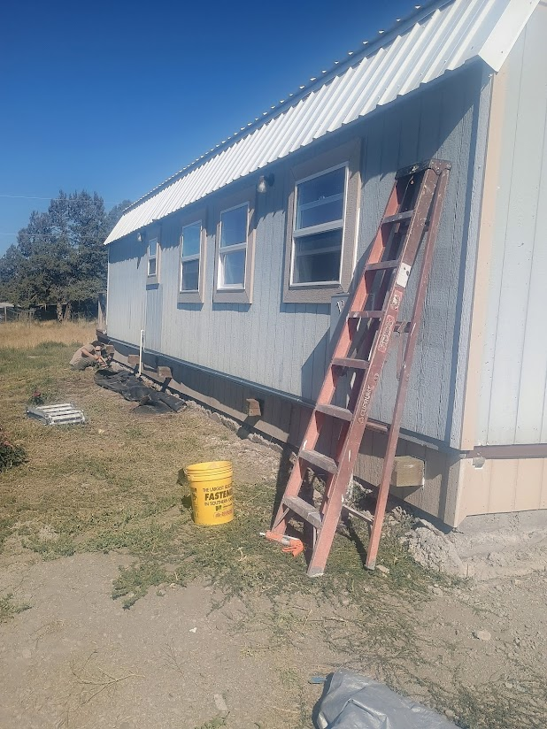 Exterior of a light blue building with a ladder leaning against it, and a yellow bucket on the ground.